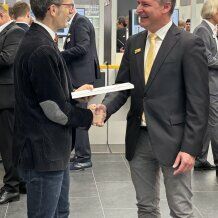 Menschen im Kontext einer Messe bei feierlicher Übergabe vom Zertifikat