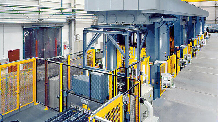 A large plant containing yellow elements stands in a production hall.